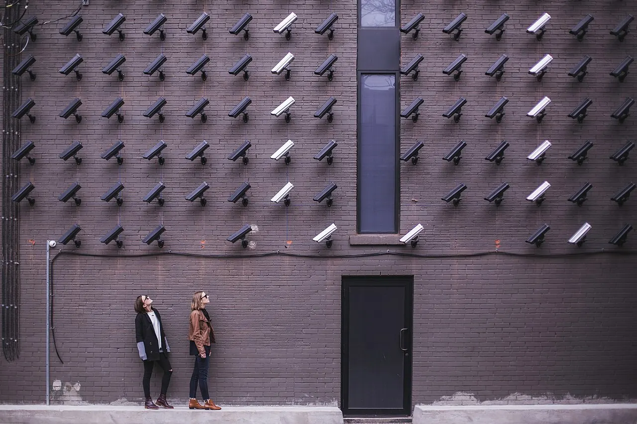 Dos personas miran una pared cubierta de decenas de cámaras de vigilancia